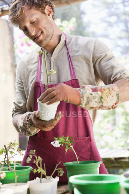 Mann in Schürze pflanzt Blumen in Töpfen im Freien — Stockfoto