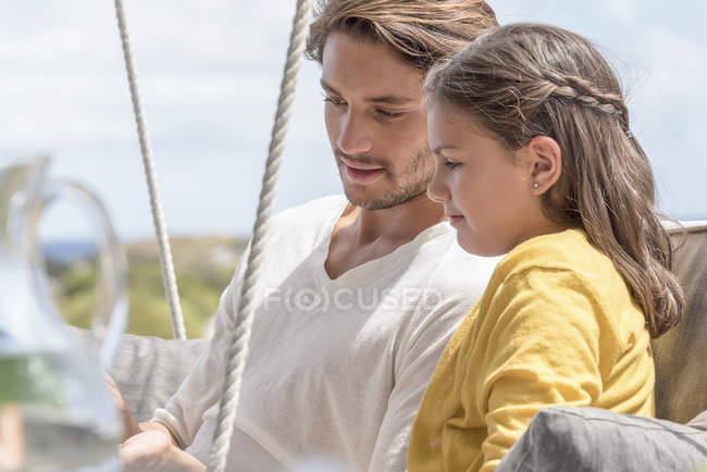Feliz padre con hija pequeña sentados juntos en la silla oscilante - foto de stock