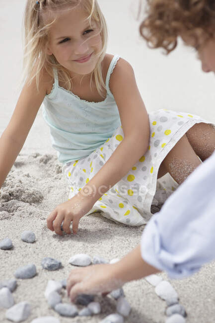Hermanos jugando con guijarros en la playa - foto de stock