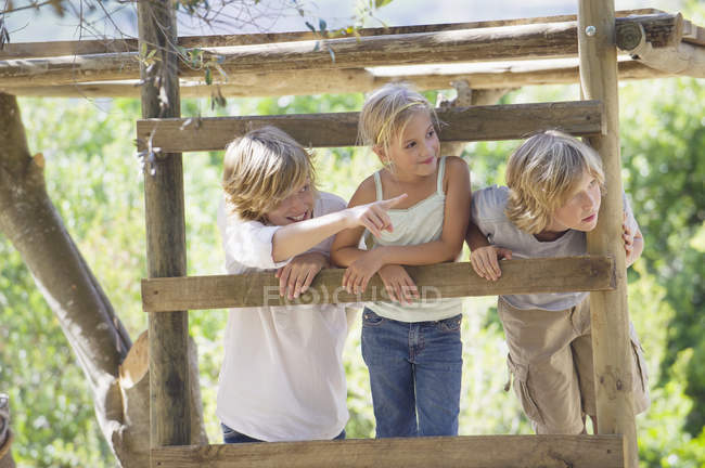 Усміхнені діти, дивлячись далеко від дерев'яного будинку в літньому саду — стокове фото