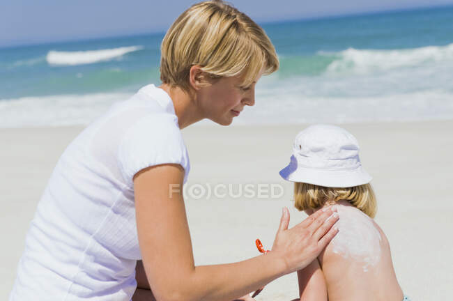 Donna che applica lozione abbronzatura a sua figlia sulla spiaggia — Foto stock