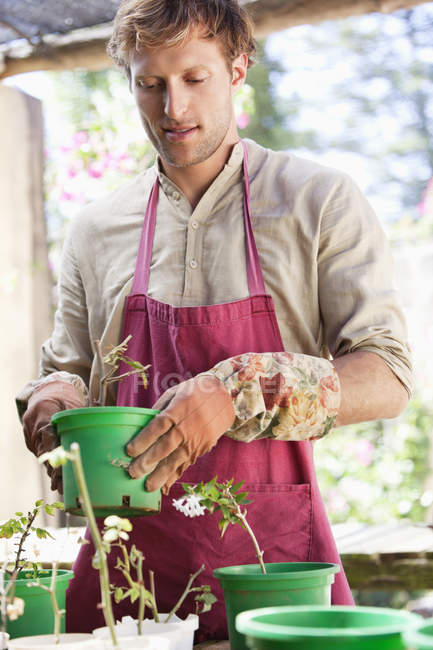 Homem de avental plantando flores em vasos ao ar livre — Fotografia de Stock