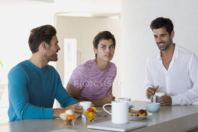 Primer plano de tres amigos tomando café y sonriendo - foto de stock