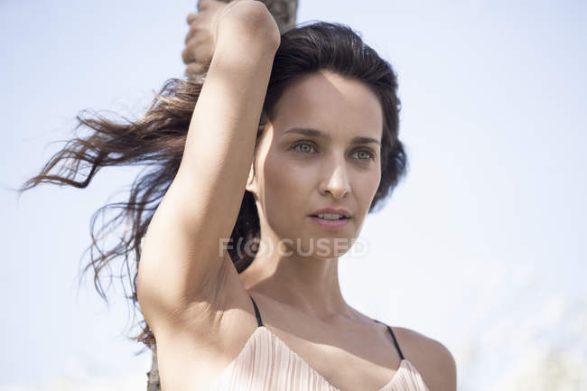Thoughtful woman leaning on tree trunk against sky — Stock Photo