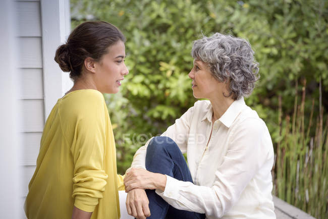 Madre hablando con hija adulta en el porche - foto de stock