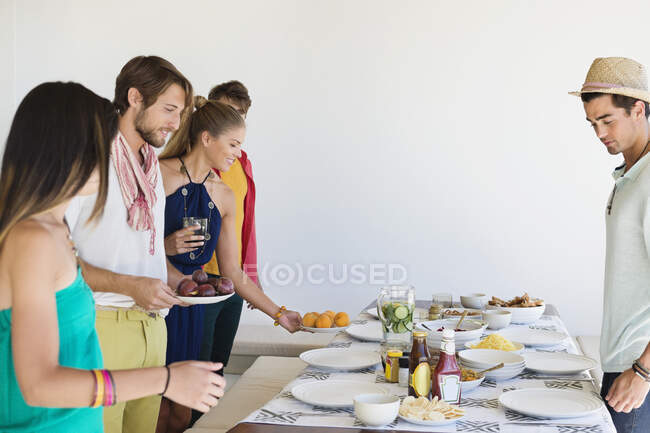 Amigos organizando comida em uma mesa de jantar — Fotografia de Stock
