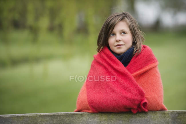 Portrait of smiling girl wrapped in blanket standing in field on blurred background — Stock Photo