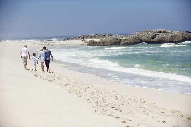 Vista trasera de una familia de varias generaciones caminando por la playa - foto de stock