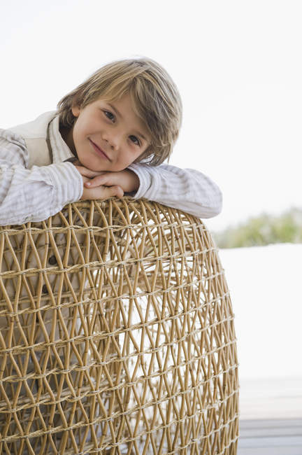 Портрет улыбающегося мальчика, опирающегося на плетеное кресло — стоковое фото
