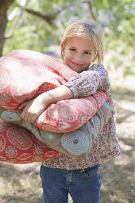Porträt eines lächelnden kleinen Mädchens, das Kissen im Freien trägt — Stockfoto