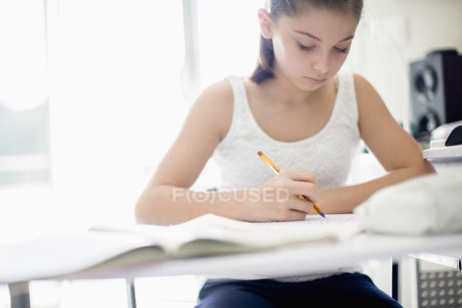Chica adolescente enfocada estudiando en el escritorio - foto de stock