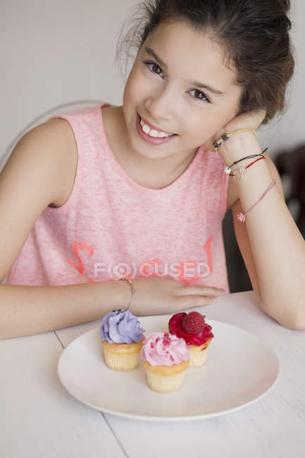 Sorrindo menina sentada em cupcakes na mesa e olhando para a câmera — Fotografia de Stock