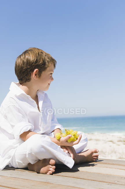 Petit garçon assis sur une promenade en bois sur la côte de la mer — Photo de stock