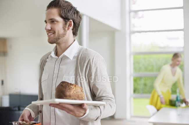 Uomo sorridente che porta il pane sul vassoio a casa — Foto stock
