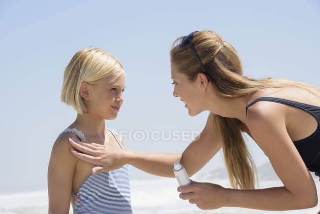 Красивая женщина наносит солнцезащитный крем на тело дочери — стоковое фото
