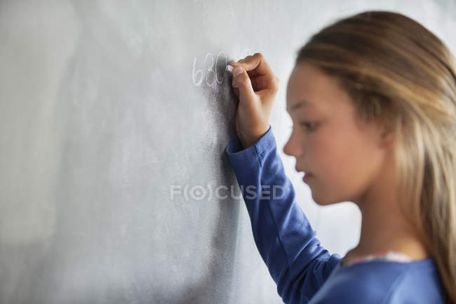 Primer plano de la adolescente escribiendo en pizarra en un aula - foto de stock