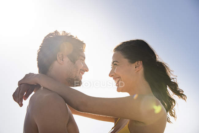 Feliz joven pareja abrazándose contra el cielo despejado - foto de stock