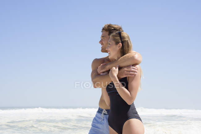 Uomo abbracciando moglie sulla spiaggia sotto il cielo blu — Foto stock