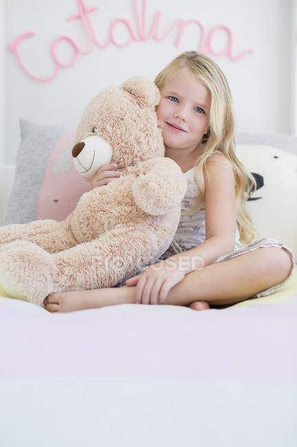 Портрет улыбающейся милой девочки, держащей плюшевого мишку на кровати — стоковое фото