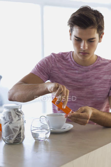 Primer plano del hombre joven que toma tabletas vitamínicas en la mesa en casa - foto de stock