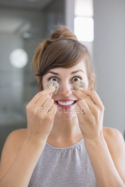 Porträt einer fröhlichen jungen Frau, die Teebeutel vor Augen hält — Stockfoto