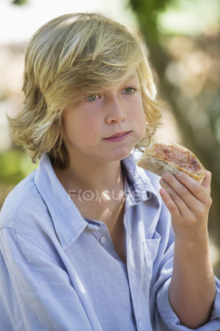 Ragazzo con i capelli biondi mangiare sandwich all'aperto — Foto stock