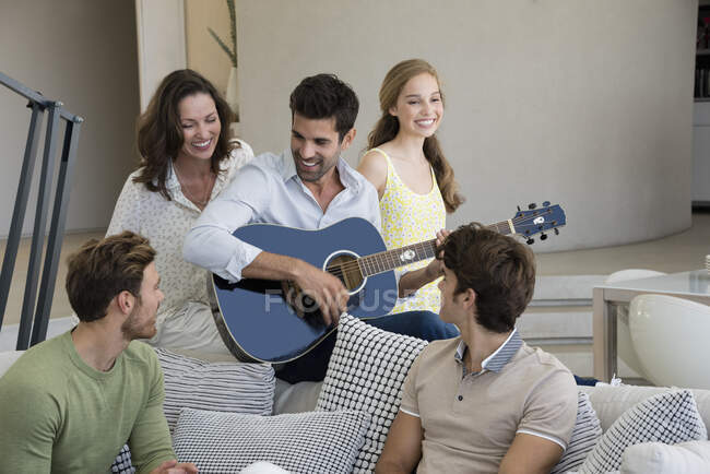 Homem tocando guitarra para seus amigos em casa — Fotografia de Stock