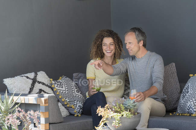 Happy couple sitting on couch and holding glasses of vegetable juice — Stock Photo