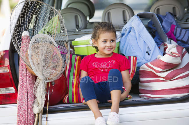 Menina bonito sentado no porta-malas do carro com coisas para férias — Fotografia de Stock
