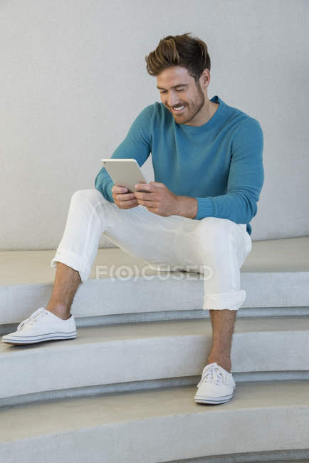 Glücklicher junger Mann mit digitalem Tablet auf der Treppe zu Hause — Stockfoto