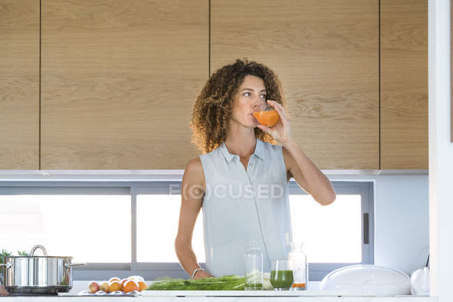 Женщина пьет морковный сок из стекла на кухне — стоковое фото