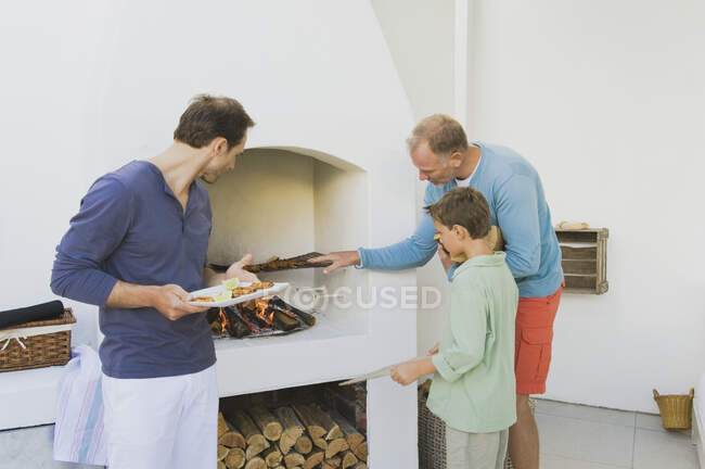 Dois homens com um menino cozinhando kebab na lareira — Fotografia de Stock