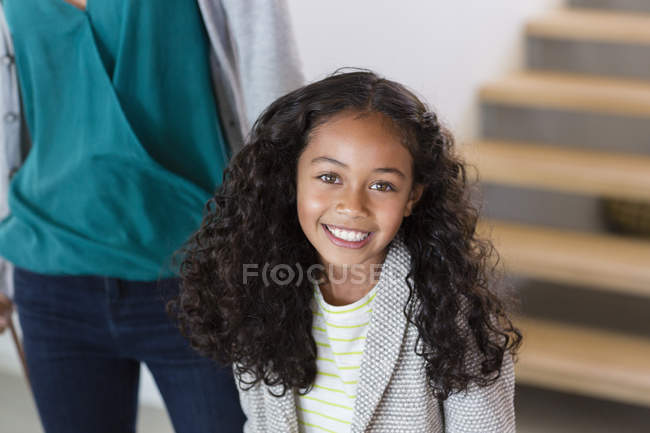Retrato de niña feliz de pie en casa con la madre en el fondo - foto de stock