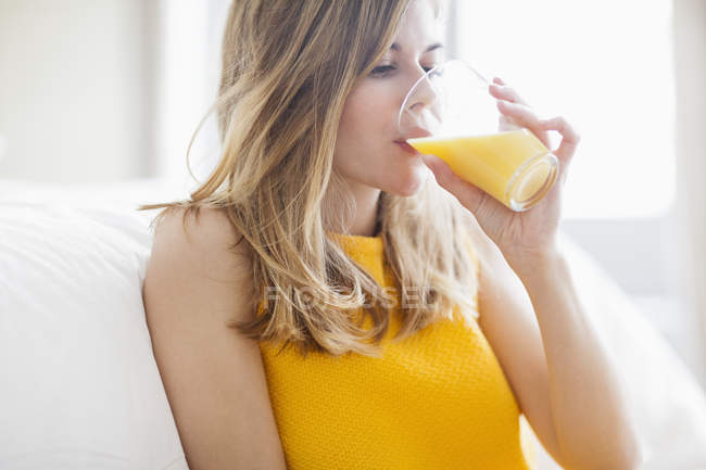 Mulher em vestido amarelo brilhante beber suco de laranja em casa — Fotografia de Stock