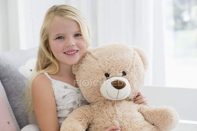 Portrait of cute little girl holding teddy bear on sofa — Stock Photo