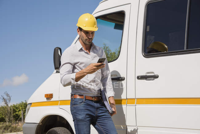 Engenheiro masculino no capacete usando telefone celular na van — Fotografia de Stock