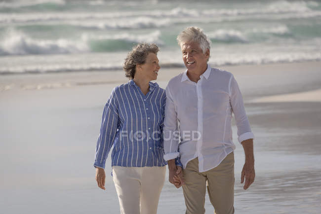 Heureux couple de personnes âgées marchant sur la plage se tenant la main — Photo de stock
