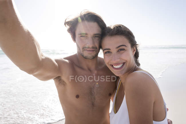 Retrato de feliz jovem casal tomando selfie na praia ensolarada — Fotografia de Stock