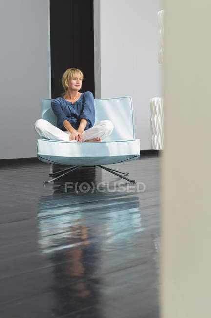 Розслаблена зріла жінка сидить на дивані в квартирі — стокове фото