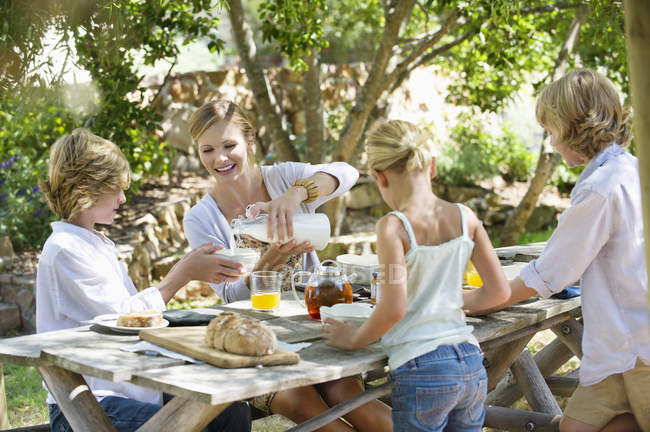 Feliz madre e hijos teniendo comida en el patio trasero de verano - foto de stock