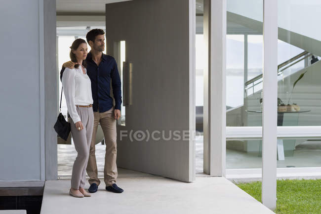Couple standing at doorway of house and looking away — Stock Photo