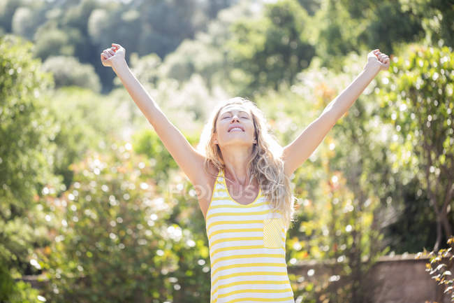 Happy woman with arms outstretched and eyes closed standing in garden — Stock Photo