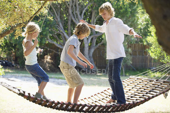 Petits frères et sœurs debout dans l'hamac dans le jardin d'été — Photo de stock