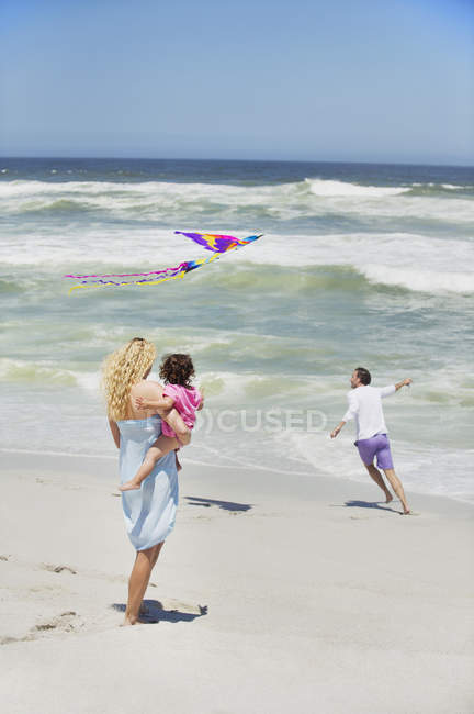 Мати носить дитину під час польоту на пляжі з повітряним змієм — стокове фото