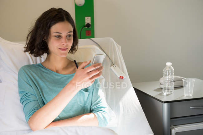 Жінка-пацієнтка, що сидить на лікарняному ліжку та текстових повідомленнях — стокове фото