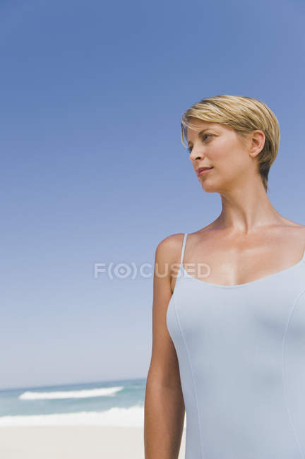 Woman with short hair standing on beach against blue sky — water, hairstyle  - Stock Photo | #222924666