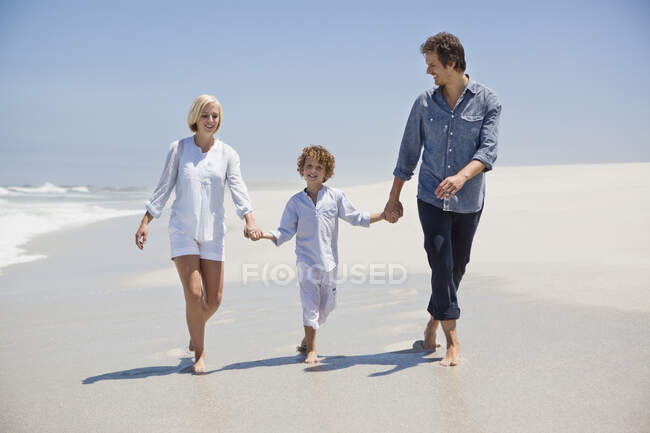 Pareja caminando en la playa con su hijo - foto de stock