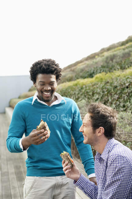 Two friends eating sandwiches on a boardwalk — Stock Photo