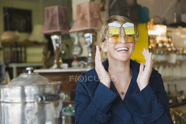 Femme souriante aux cheveux courts portant des lunettes de soleil drôles en magasin — Photo de stock
