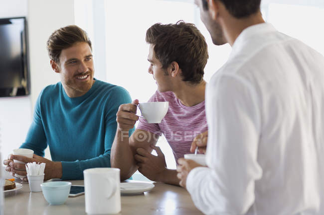 Primo piano di tre amici che bevono caffè in cucina — Foto stock